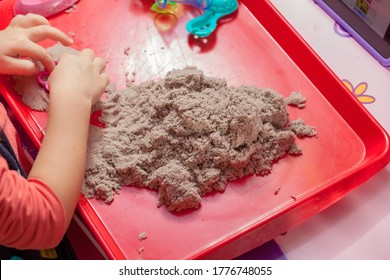 Little Hands Playing With Kinetic Sand And Molds On The Red Tray
