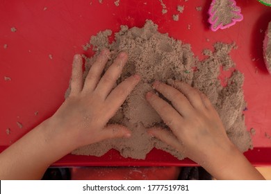 Little Hands Playing With Kinetic Sand And Molds On The Red Tray