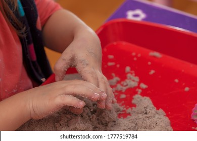 Little Hands Playing With Kinetic Sand And Molds On The Red Tray