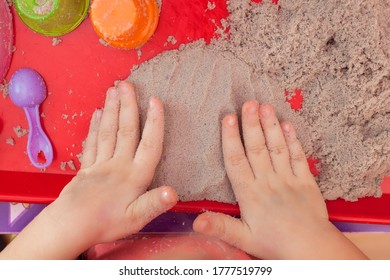 Little Hands Playing With Kinetic Sand And Molds On The Red Tray
