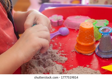 Little Hands Playing With Kinetic Sand And Molds On The Red Tray
