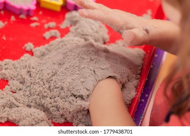 Little Hands Playing With Kinetic Sand And Molds On The Red Tray