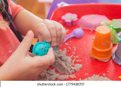 Little Hands Playing With Kinetic Sand And Molds On The Red Tray
