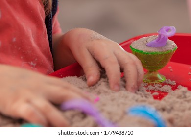 Little Hands Playing With Kinetic Sand And Molds On The Red Tray