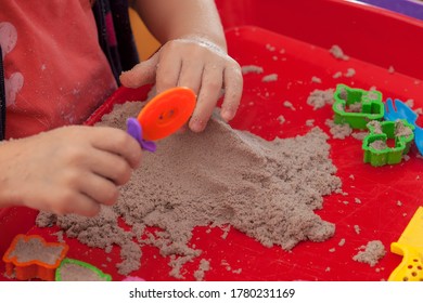 Little Hands Playing With Kinetic Sand And Molds On The Red Tray