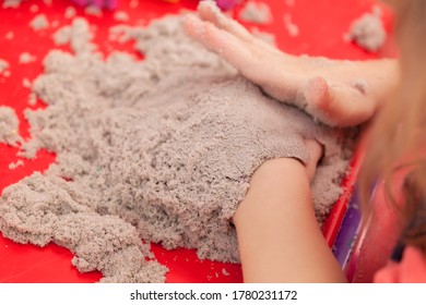 Little Hands Playing With Kinetic Sand And Molds On The Red Tray