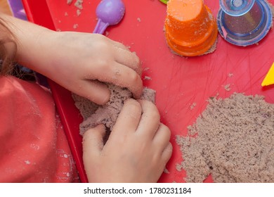 Little Hands Playing With Kinetic Sand And Molds On The Red Tray
