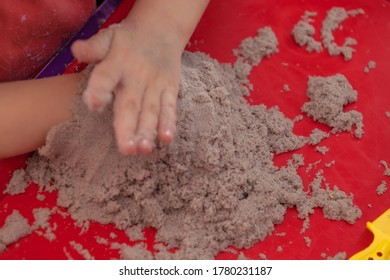 Little Hands Playing With Kinetic Sand And Molds On The Red Tray