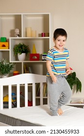 A little handsome boy of 4-5 years jumps on a wooden bed on a mattress, vertical photo