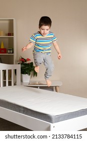 A little handsome boy of 4-5 years jumps on a wooden bed on a mattress, vertical photo