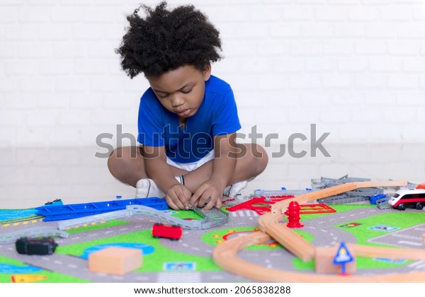 Little happy black people\
African American child playing with a railroad train toy in the\
living room.