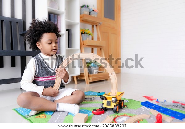 Little happy black people\
African American child playing with a railroad train toy in the\
living room.