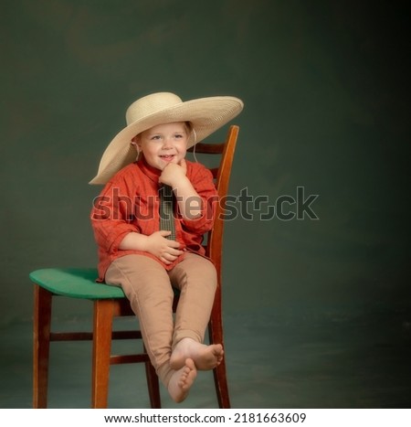 little happy  boy in big hat and red shirt on old chair  on dark green background