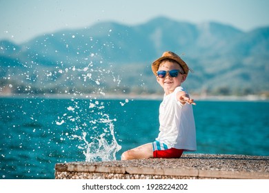 Little Happy Boy In Blue Sunglasses And Hat Has A Big Smile On His Face. Beautiful Landscape And Bright Beach. Blue Summer Sky And Sea Water Background. Kid On Summer Vacation. Text. Copy Space