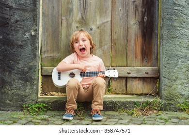Little happy boy plays his guitar or ukulele