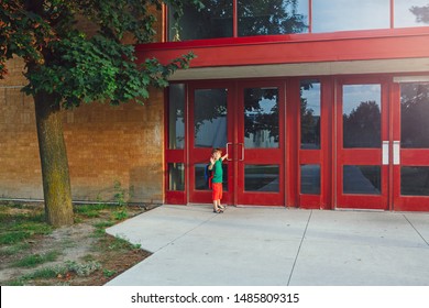 Little Happy Caucasian Boy Student Kid With Backpack Waving Hand And Opening Red Door On 1 September Day. Education And Back To School Concept. Child Pupil Ready To Learn And Study. 