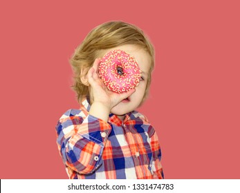 Little happy cute boy is eating donut on red background wall. Child is having fun with donut. Tasty food for playing kids. Funny time  with sweet food. Bright baby boy in a plaid shirt.