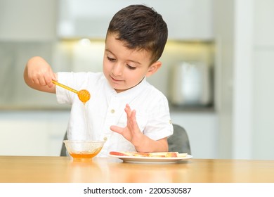 Little happy cute boy eating apple with honey, holding honey dipper. Child is having fun, celebrate Jewish New Year Rosh Hashanah.