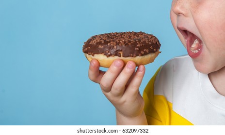 Little happy cute boy is eating donut on blue background wall. child is having fun with donut. Tasty food for kids. Funny time at home with sweet food. Bright kid. Donut with chocolate. 