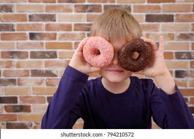Little happy cute boy is posing with donuts on brick wall background