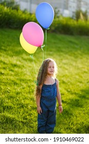 Little happy girl having fun and playing with her beautiful hair and balloons in the park in spring. Happy childhood. Fun little girl on a walk in the park in spring.