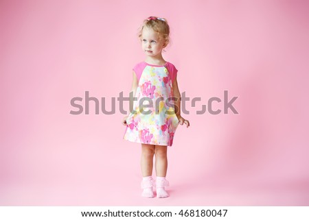 little happy girl in pink colored dress with blonde hair on pink background in Studio