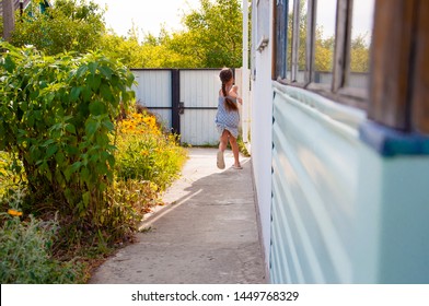 Little Happy Girl Running Around The Corner Of A House In A Summer Village