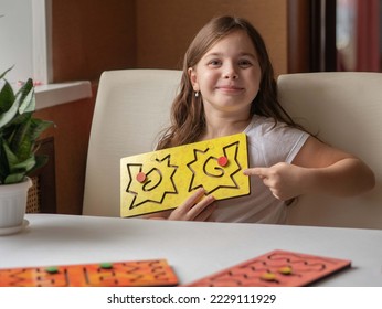 A little happy girl smiles and holds up an interhemispheric board for remedial classes with speech disorders or neurology. A fashionable simulator for the psychoemotional development of children.