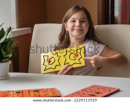 A little happy girl smiles and holds up an interhemispheric board for remedial classes with speech disorders or neurology. A fashionable simulator for the psychoemotional development of children.