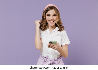 Little happy kid girl 12-13 year old in white shirt using mobile cell phone chat online do winner gesture clench fist isolated on purple background children studio portrait Childhood lifestyle concept - Shutterstock ID 2115173834