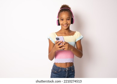 Little happy kid teen girl of African American ethnicity 13-14 years old wear casual hoody hat headphones listen music use mobile cell phone isolated on white background Childhood concept - Powered by Shutterstock