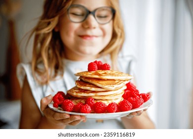 Little happy preschool girl with a large stack of pancakes and raspberries for breakfast. Positive child eating healthy homemade food in the morning. - Powered by Shutterstock