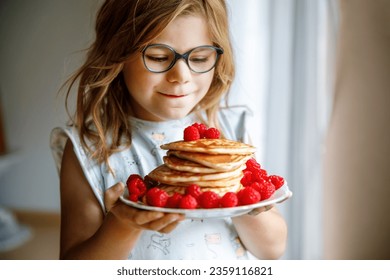 Little happy preschool girl with a large stack of pancakes and raspberries for breakfast. Positive child eating healthy homemade food in the morning. - Powered by Shutterstock