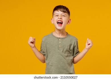 Little Happy Small Fun Happy Child Kid Boy 6-7 Years Old Wearing Green T-shirt Do Winner Gesture Clench Fist Celebrate Isolated On Plain Yellow Background. Mother's Day Love Family Lifestyle Concept