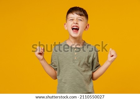 Little happy small fun happy child kid boy 6-7 years old wearing green t-shirt do winner gesture clench fist celebrate isolated on plain yellow background. Mother's Day love family lifestyle concept