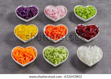 Little heart-shaped white bowls with grated vegetables of different colors. Healthy food diet studio shot concept