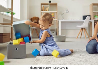 Little helper cleaning up and learning to be independent. Cute 2 year old child putting cubes back in their place after playing. Toddler boy putting toys away sitting on warm floor in nursery room