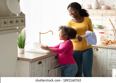 Little Helper. Cute Black Preschool Girl Washing Dishes After Lunch With Mom In Kitchen, Adorable African American Female Child Helping To Her Mother With Household At Home, Free Space