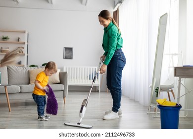 Little Helper. Mother And Her Toddler Son Doing The Cleaning Together In Living Room Interior, Kid Boy Giving Mom A Rag While Woman Washing The Floor With Mop