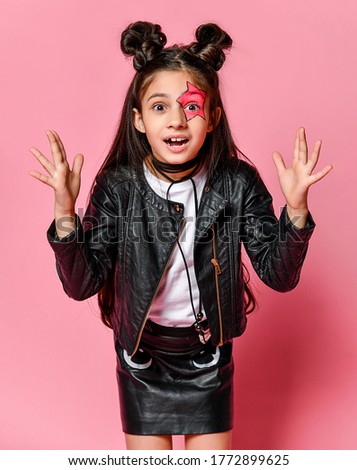 little hipster girl with a funny hairstyle and a star on her face, in a leather jacket - looking excitedly into the camera