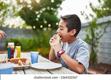 little hispanic boy eating hot dog at family bbq outside in yard