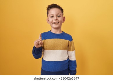 Little hispanic boy standing over yellow background smiling with an idea or question pointing finger up with happy face, number one  - Powered by Shutterstock