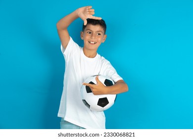 Little hispanic boy wearing white T-shirt holding a football ball making finger frame with hands. Creativity and photography concept. - Powered by Shutterstock