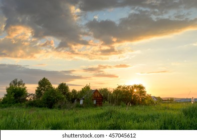 Little house in the middle of green field at the sunset behind the forest.