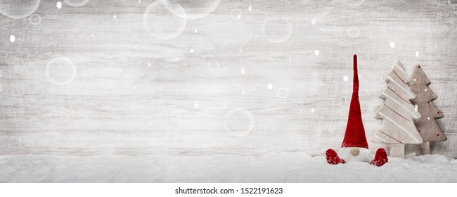 a little imp or santa claus figure sit in the snow next to two decoration christmas trees on a wooden texture background with bubbles - Shutterstock ID 1522191623