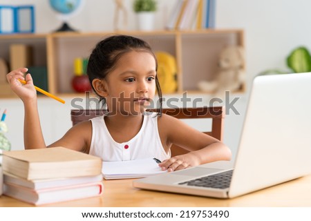 Little Indian girl looking at the laptop while doing homework
