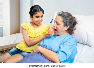 Little indian granddaughter help her grandmother patient eating apple in hospital bed. old people healthcare concept.  - Powered by Shutterstock