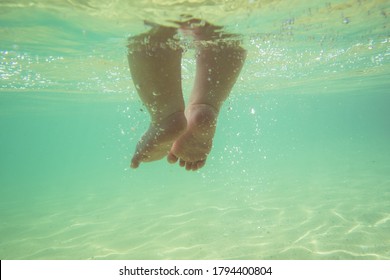 Little infant baby child legs and toes touch sand on sea beach, underwater view