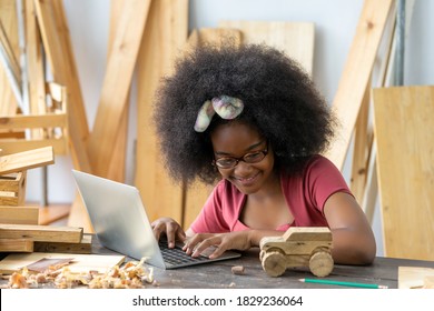 A Little Inventor Working As A Woodworker Uses The Computer To Craft Woodworking At A Workshop. African American Girl Practice To Be A Carpenter In A Carpentry Shop. DIY Crafts And Hobbies Concepts