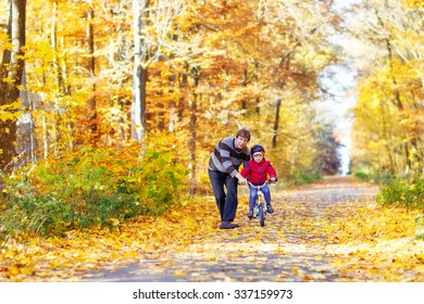 Little kid boy of 3 years and his father in autumn forest with a bicycle. Dad teaching his son. Active family leisure. Child with helmet. Safety, sports, leisure with kids concept.